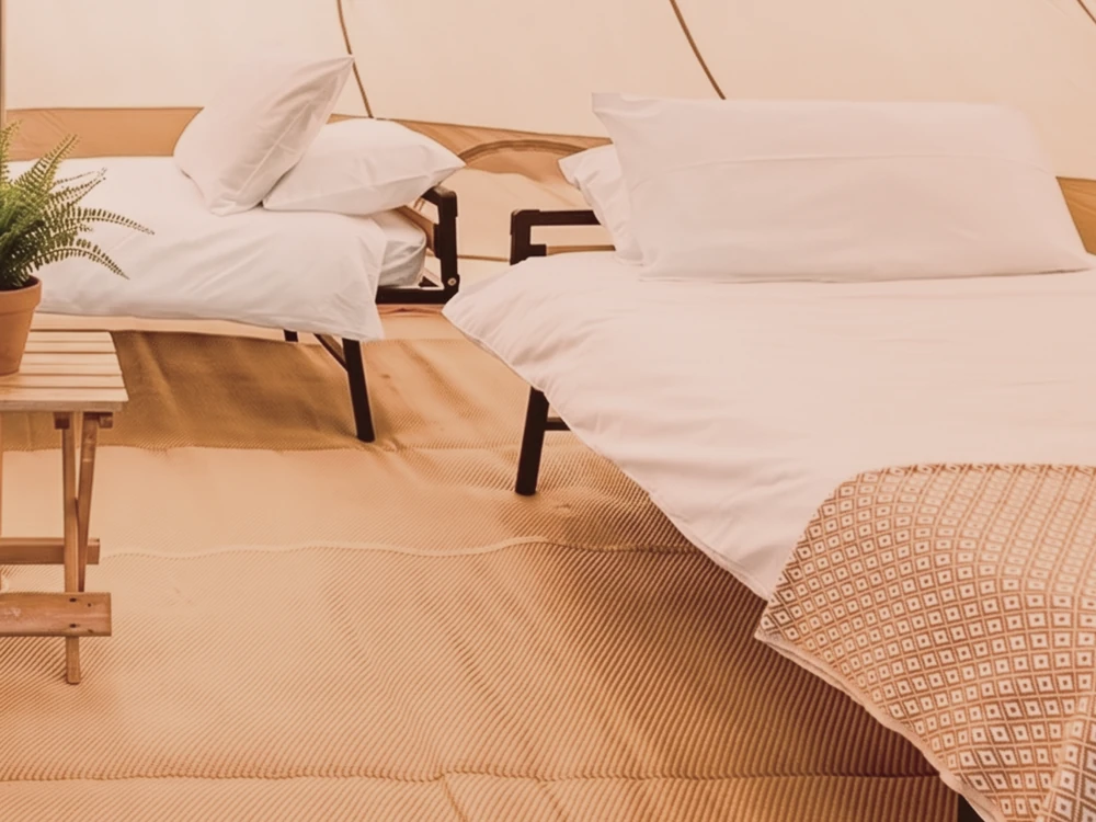 Bell tent set up with two single beds and a wooden side table with a fern.